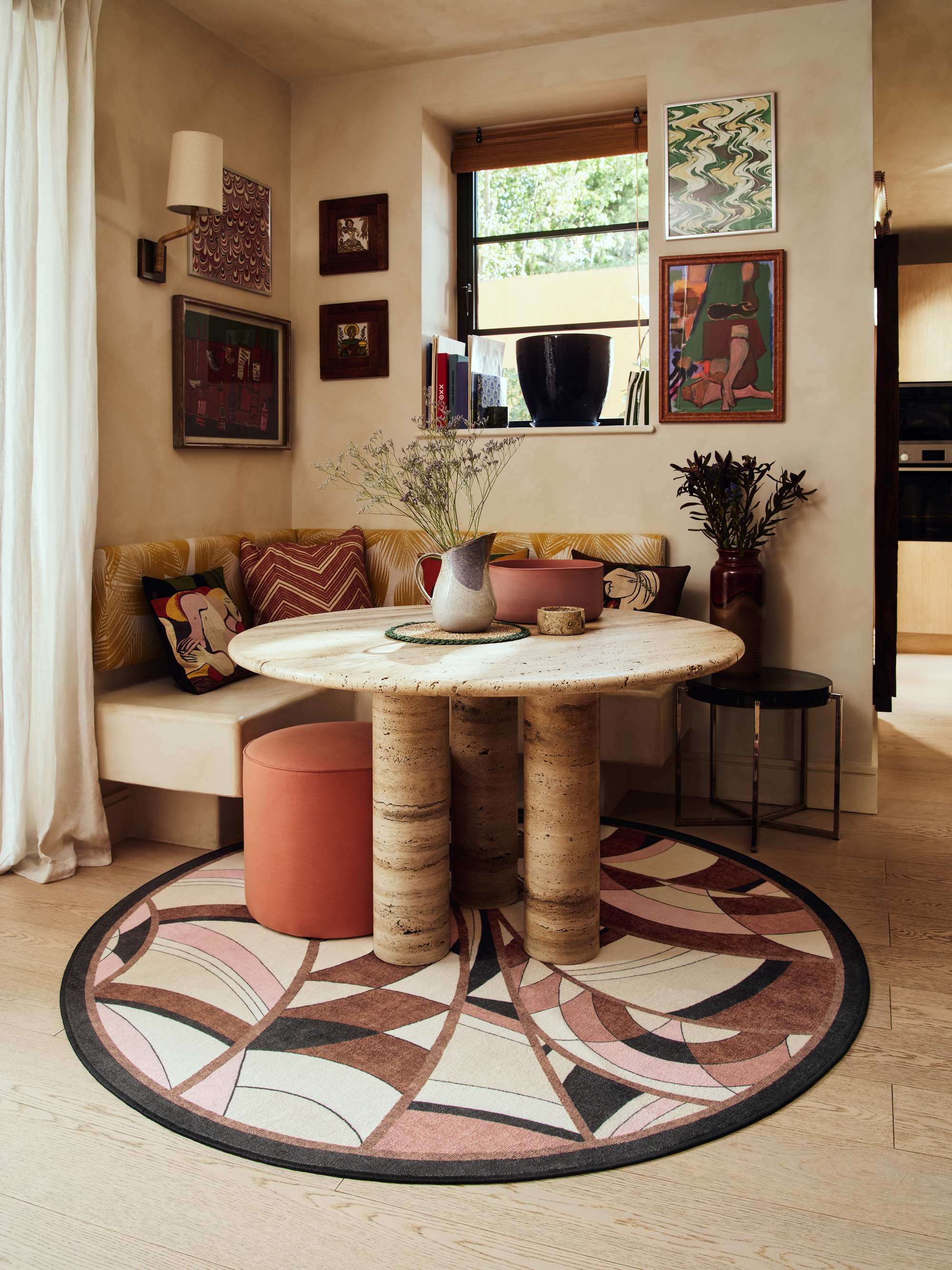 Image of a modern breakfast nook with an Art Deco print circle rug and a circular marble table. There are multiple frames hanging on the wall.