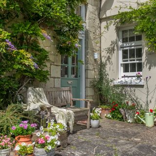 back door of a house with a garden bench and an array of planters filled with colourful flowers