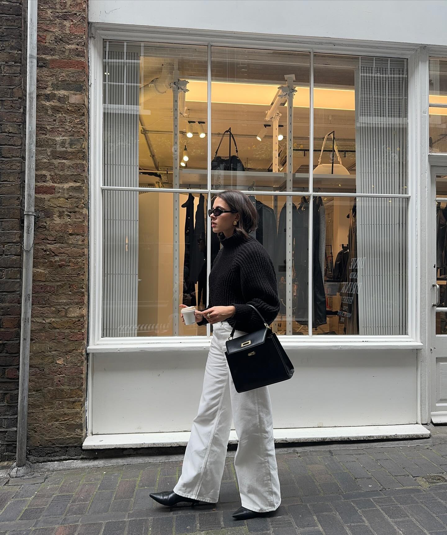 Influencer wears M&S top handle bag with white jeans and a black jumper.