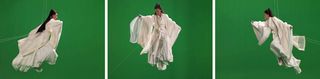 A woman wearing pale robes suspended in a flying pose in front of a green screen
