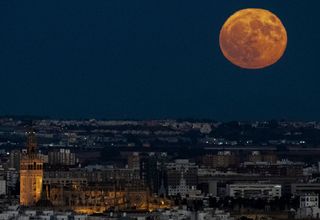 The full Moon rises over the cathedral of Seville and shines a dusty orange color.