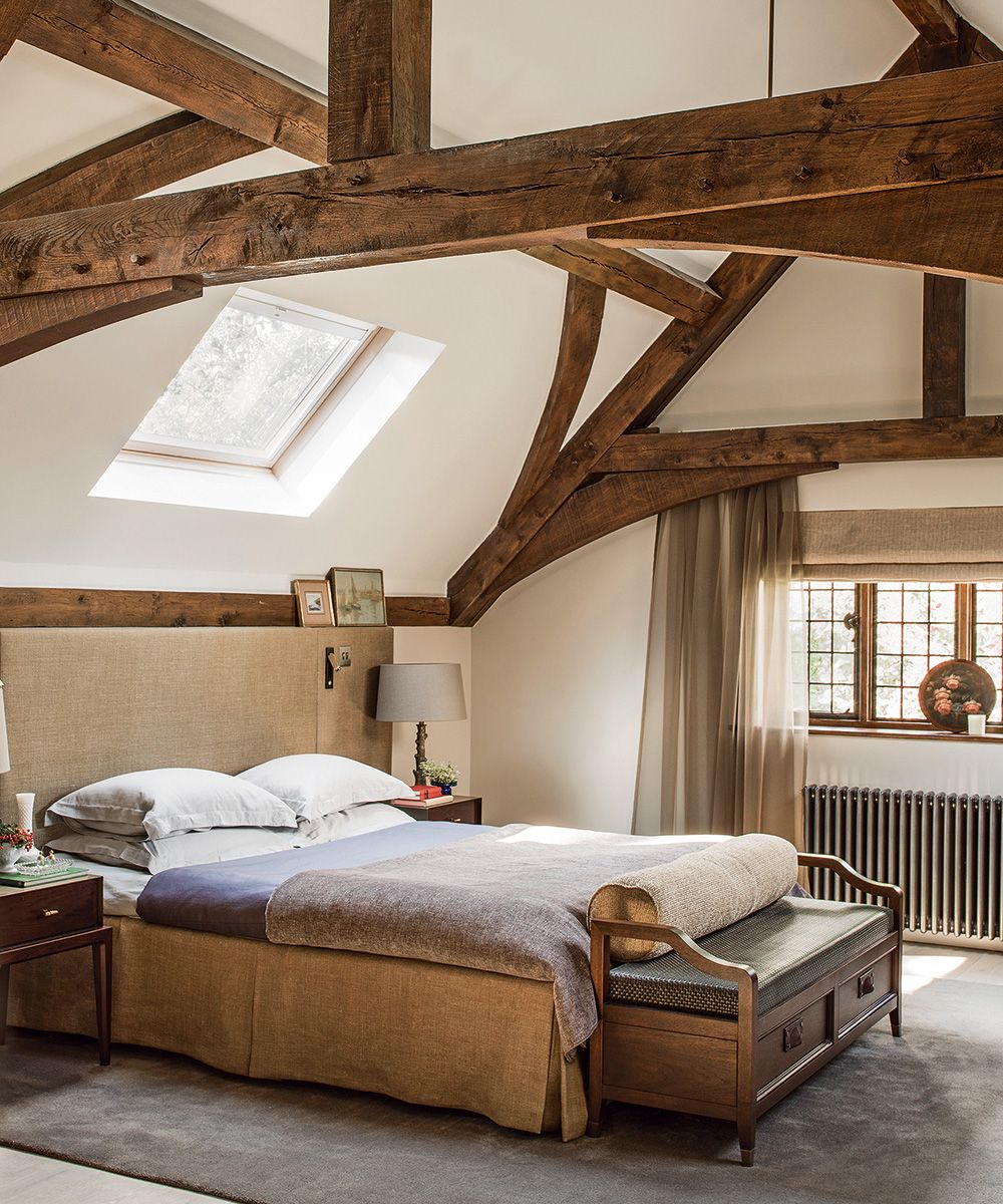 A beamed bedroom with jute upholstered bed and wooden bench seat.