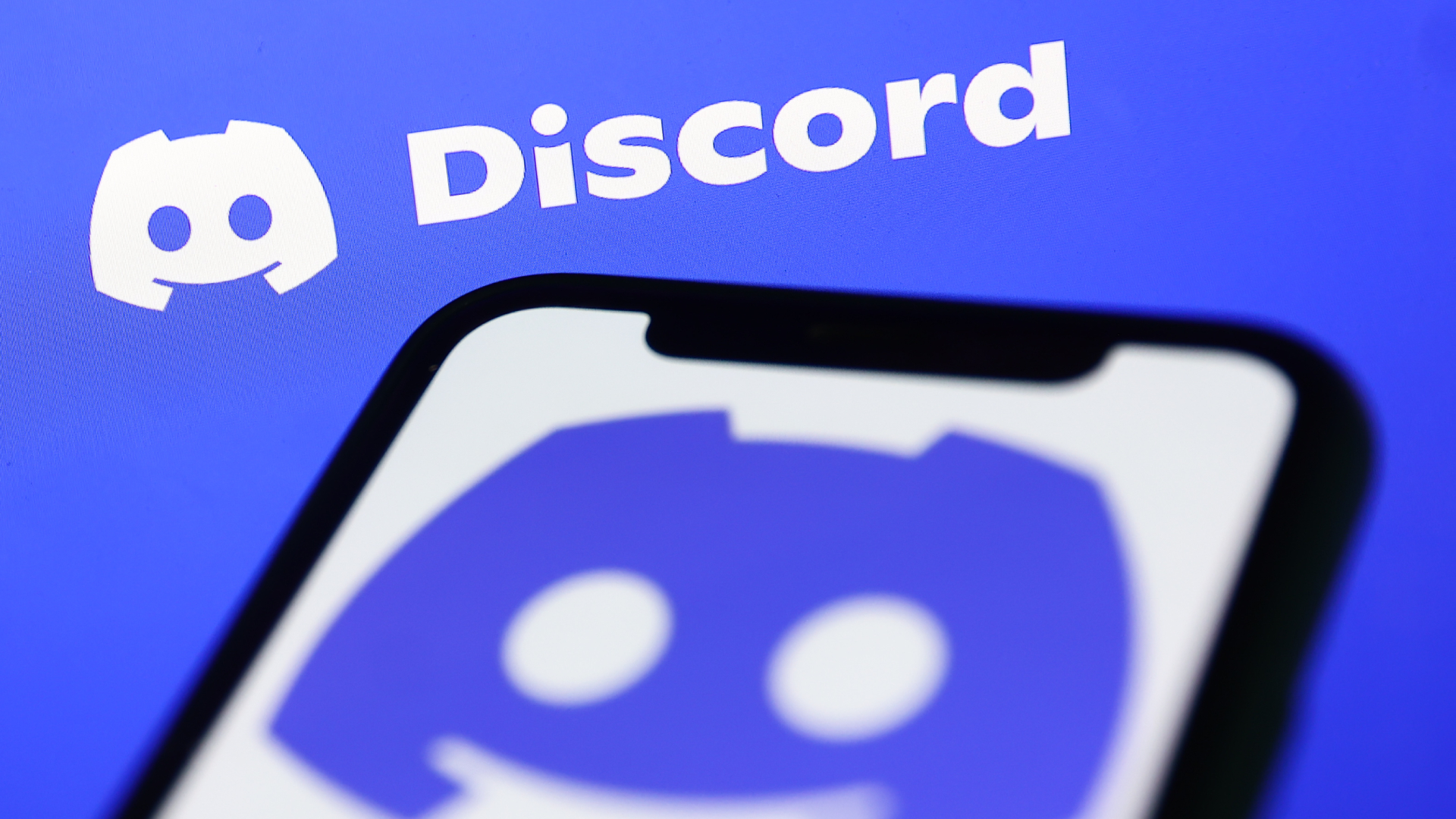 Discord logo displayed on a phone screen and Discord website displayed on a screen in the background are seen in this illustration photo taken in Krakow, Poland on November 5, 2022.
