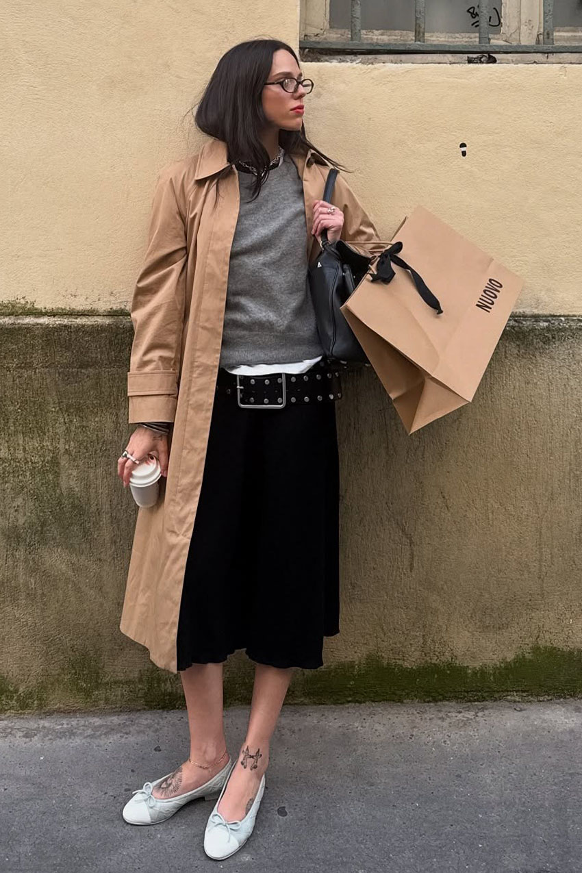 A woman wearing a gray sweater, black culottes and a tan trench coat