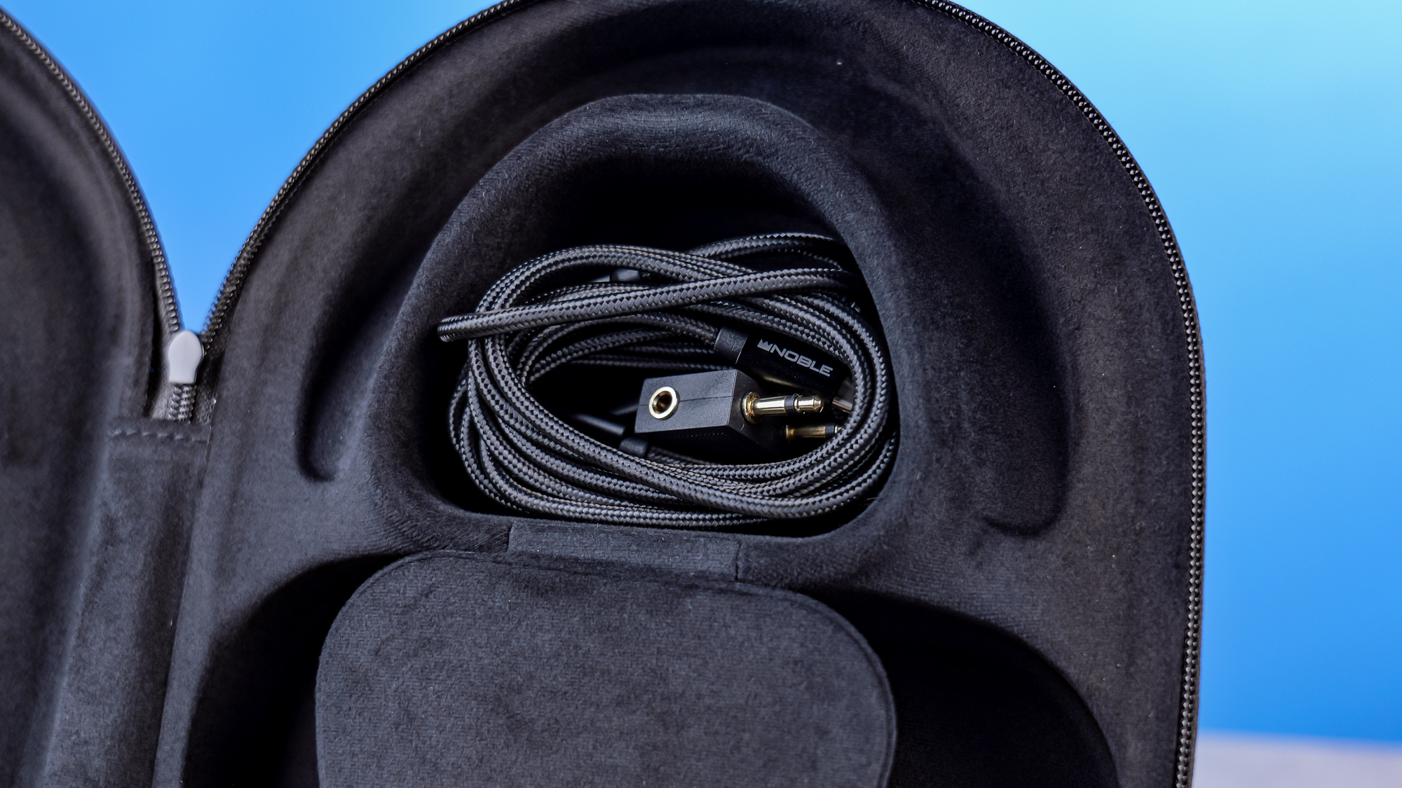The Noble Audio FoKus Artemis carry case, open showing the cable tidy compartment, against a blue background