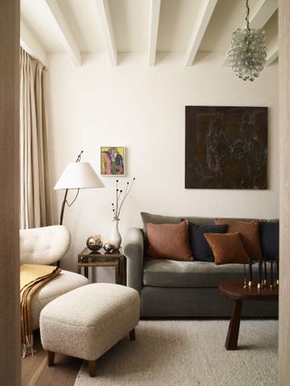 Modern living room with a sage green couch and a white bouclé accent chair in the corner