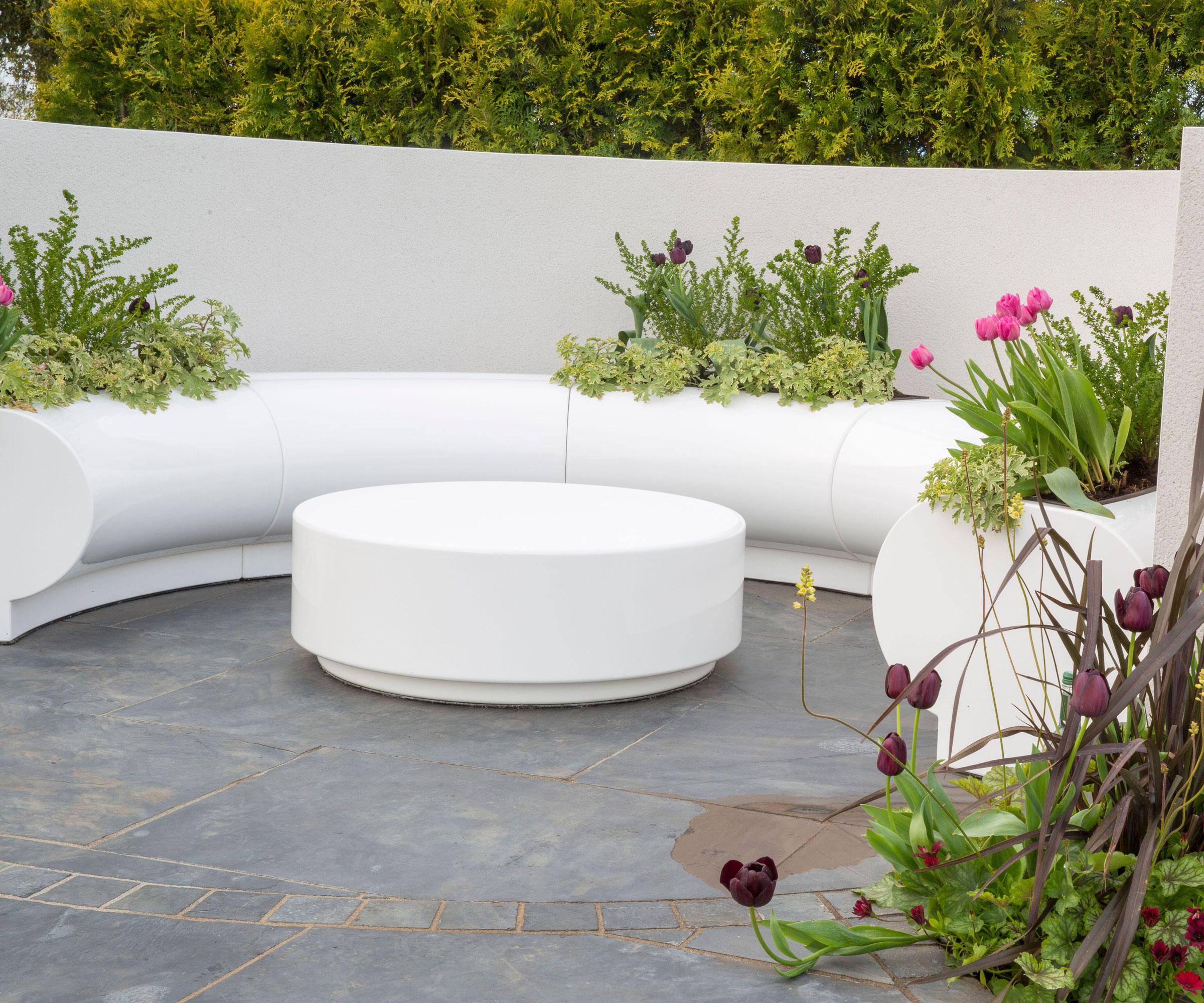 circular patio with white wall and seat, planting pockets and garden table