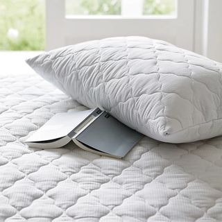 A white quilted The White Company mattress protector and pillow protector on a bed with an open book