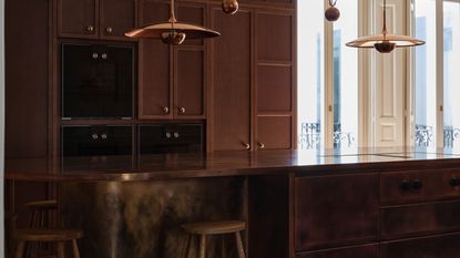 An open kitchen with copper countertop and island, copper lighting and stools