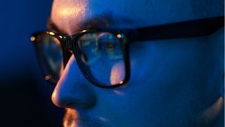Man with glasses in blue light looking at computer screen