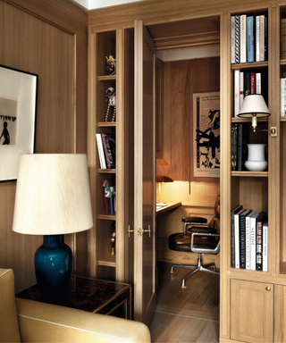 office in wooden cupboard like space with inbuilt bookshelves either side of entrance and table light in the foreground