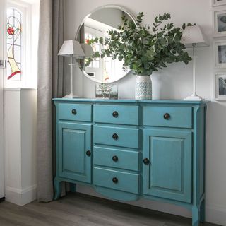 hallway with blue cabinet and round mirror
