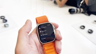 En hand som håller upp en Apple Watch Ultra med ett orange armband.