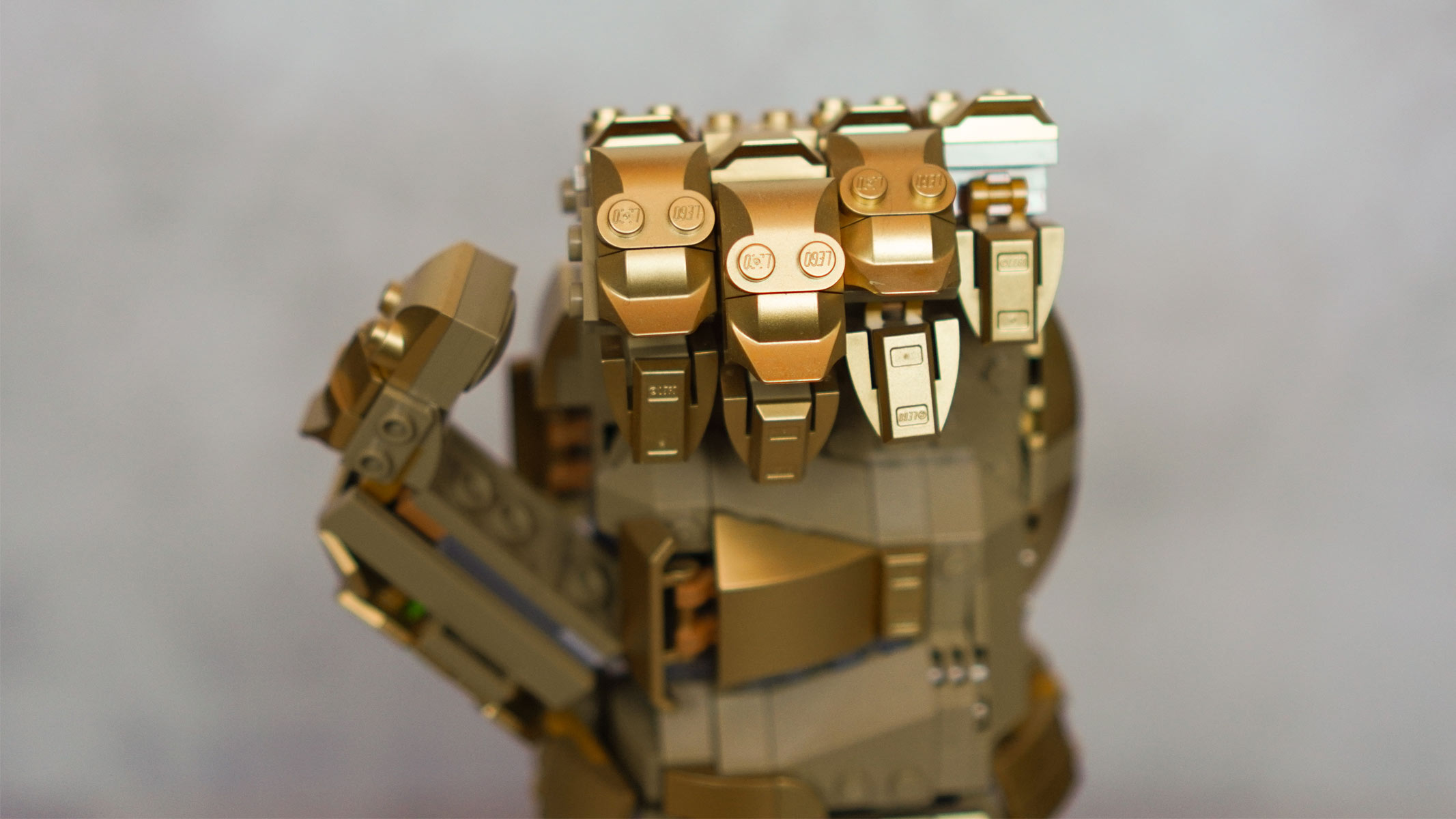 The front of a hand made of gold bricks is in a half-clenched shape and is placed in front of a grey background.