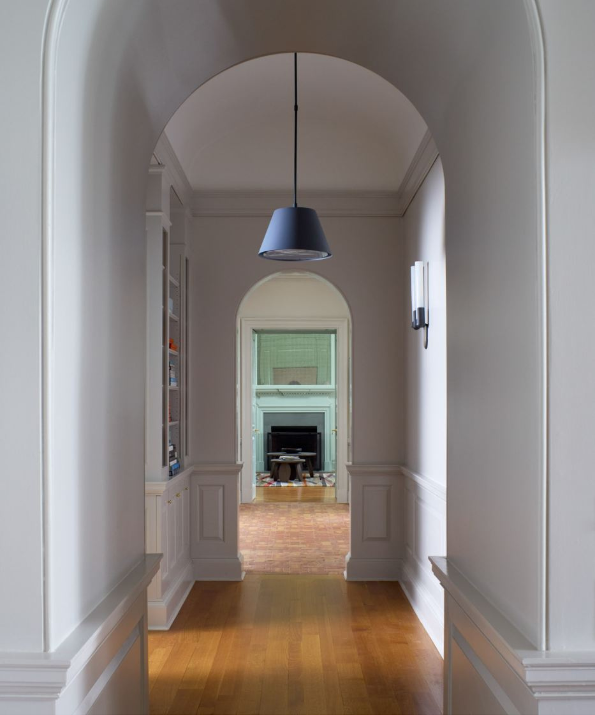 A greige, arched hallway with hardwood floors and a single navy blue light fixture hanging from the ceiling