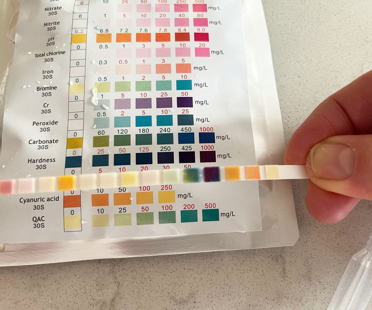 hand holding used water test strip against back of packet to show readings