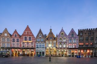 Market Square in Bruges at dusk, with picturesque historic buildings lit up and colorful.