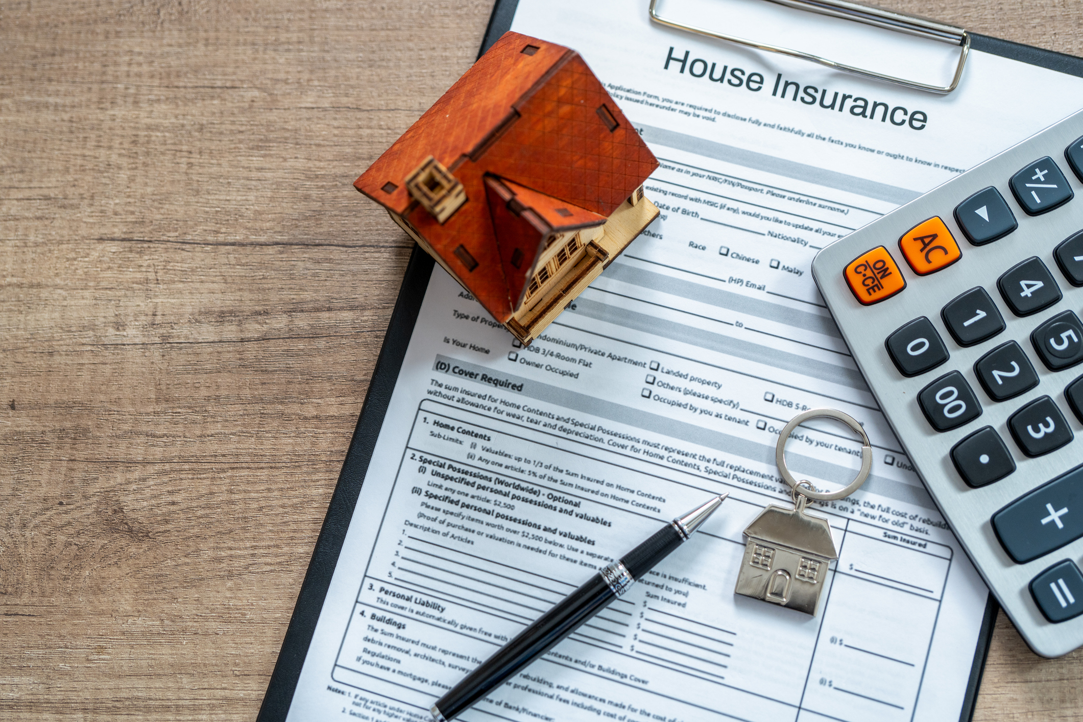 Home insurance form being filled out on a desk with a calculator and wooden house 