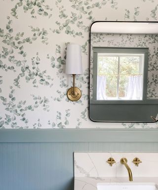 Bathroom with patterned wallpaper, white fabric sconces and wall mirror above white sink
