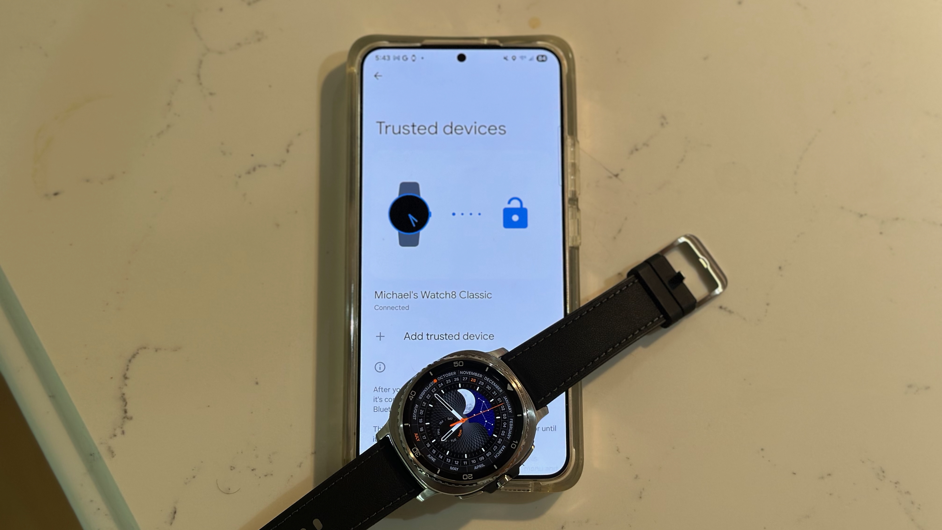 The Samsung Galaxy Watch 8 Classic sitting on a Galaxy phone showing the "Trusted devices" settings menu with the Watch 8 Classic included, for the Extend Unlock function.