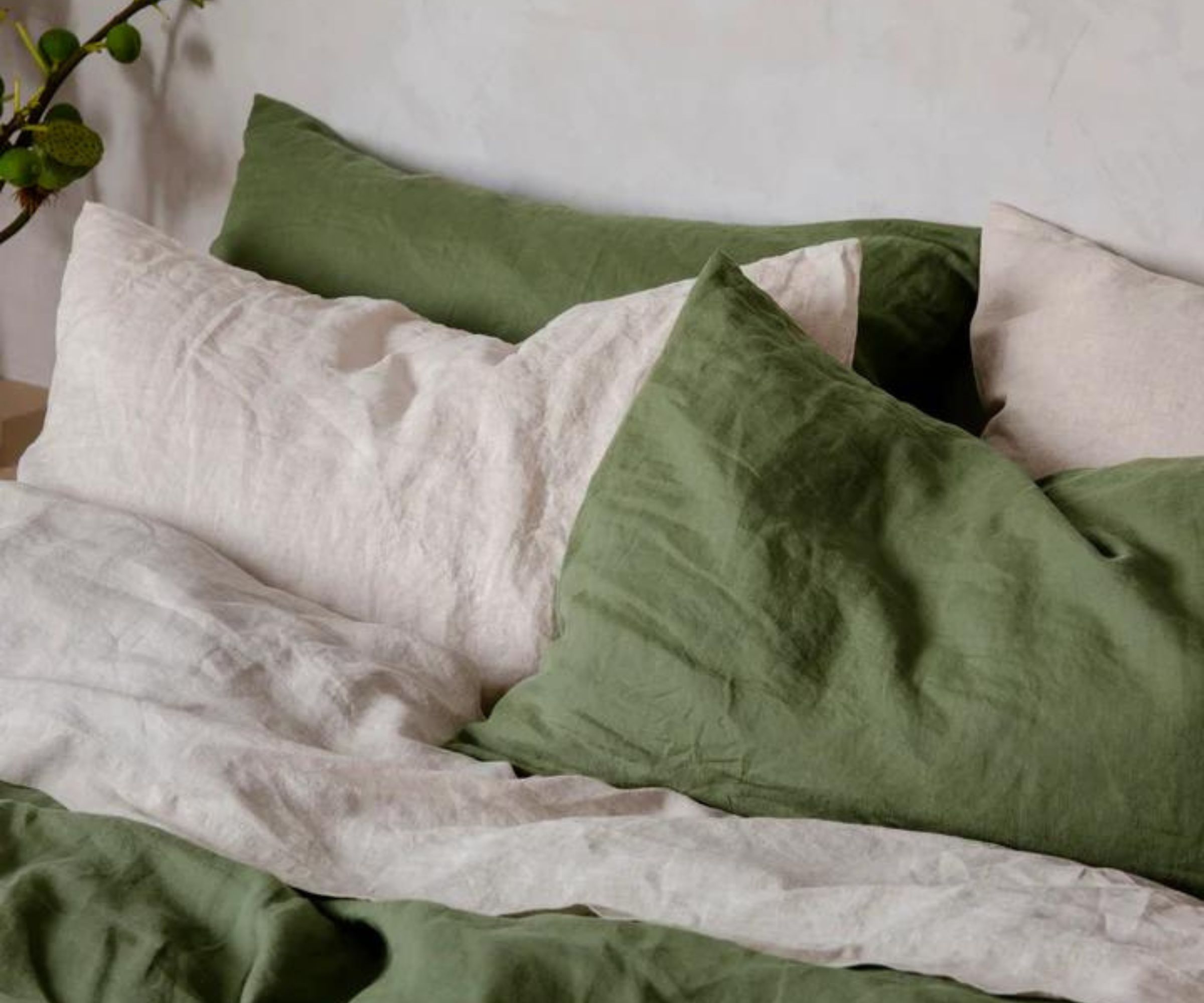 Green and white hypoallergenic bed sheets and pillowcases on a bed against a white wall.