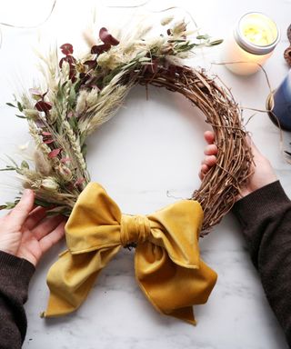 Hands making a DIY wreath with ornamental grasses and ribbon