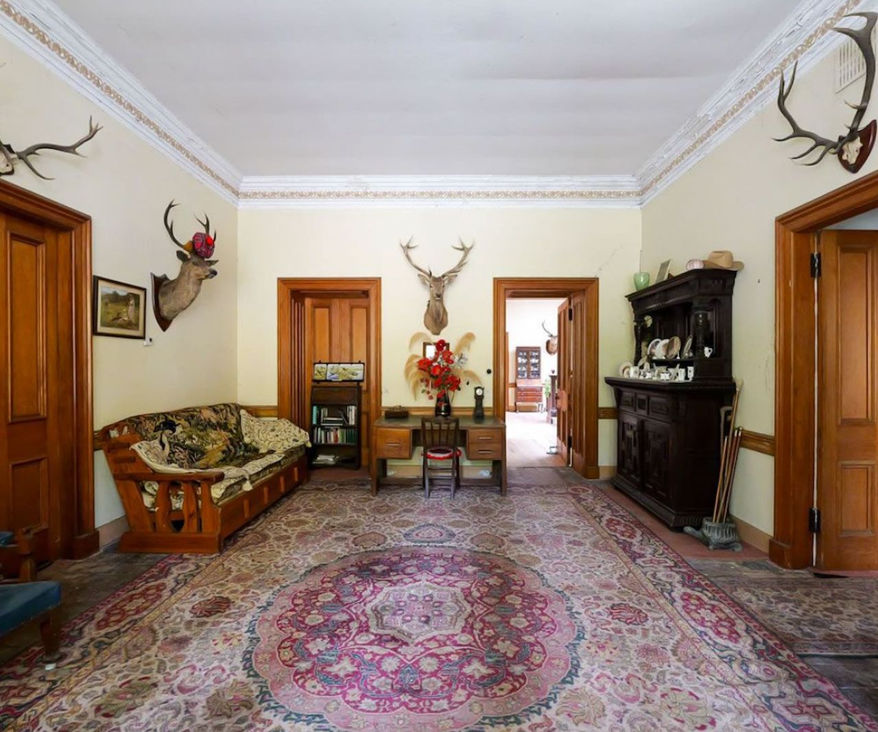 A hallway with a carpet and deer heads on the wall with many connecting doors