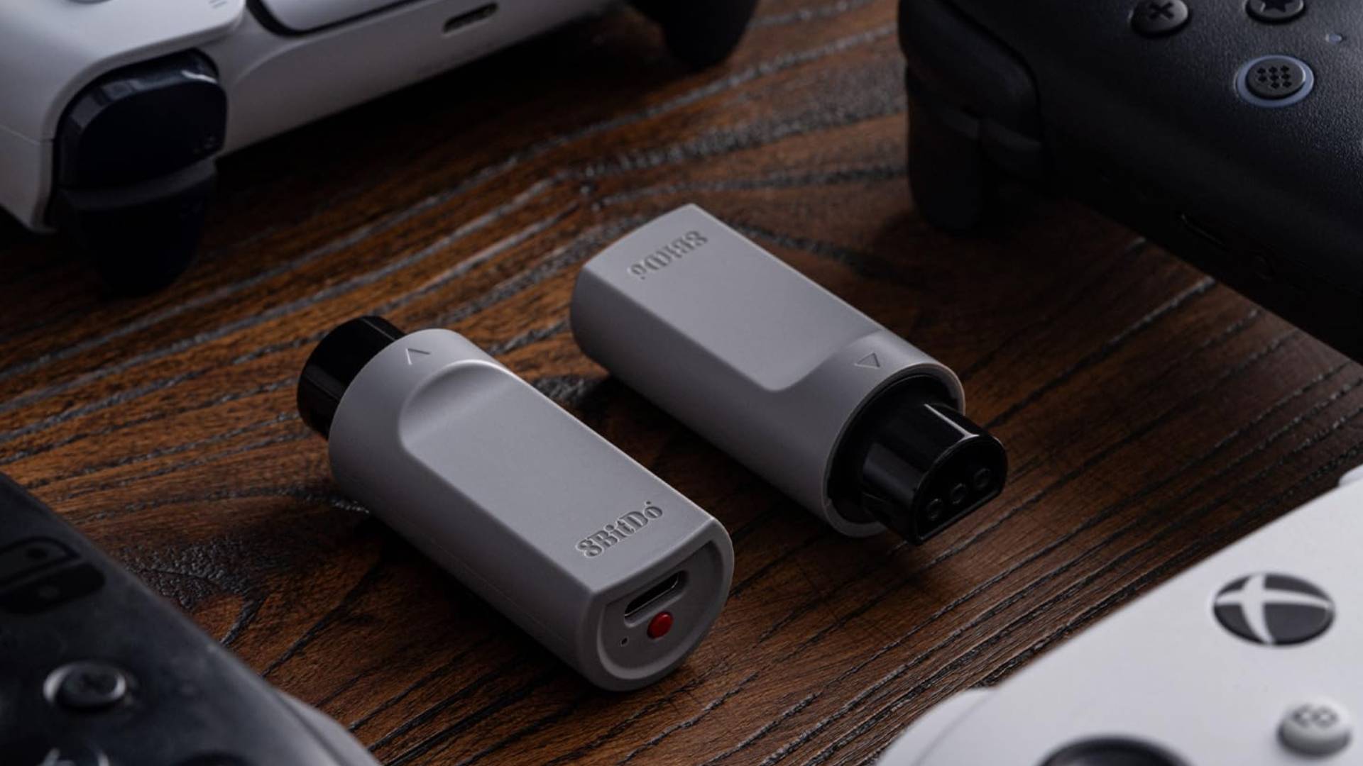 Two 8Bitdo Retro Receiver for N64 adapters sitting surrounded by modern DualSense, Xbox, Ultimate 2, and Switch Pro controllers.