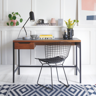 black desk and office in chair in white home office. There is a geometric blue floor runner under the chair and houseplants decorating the desk.