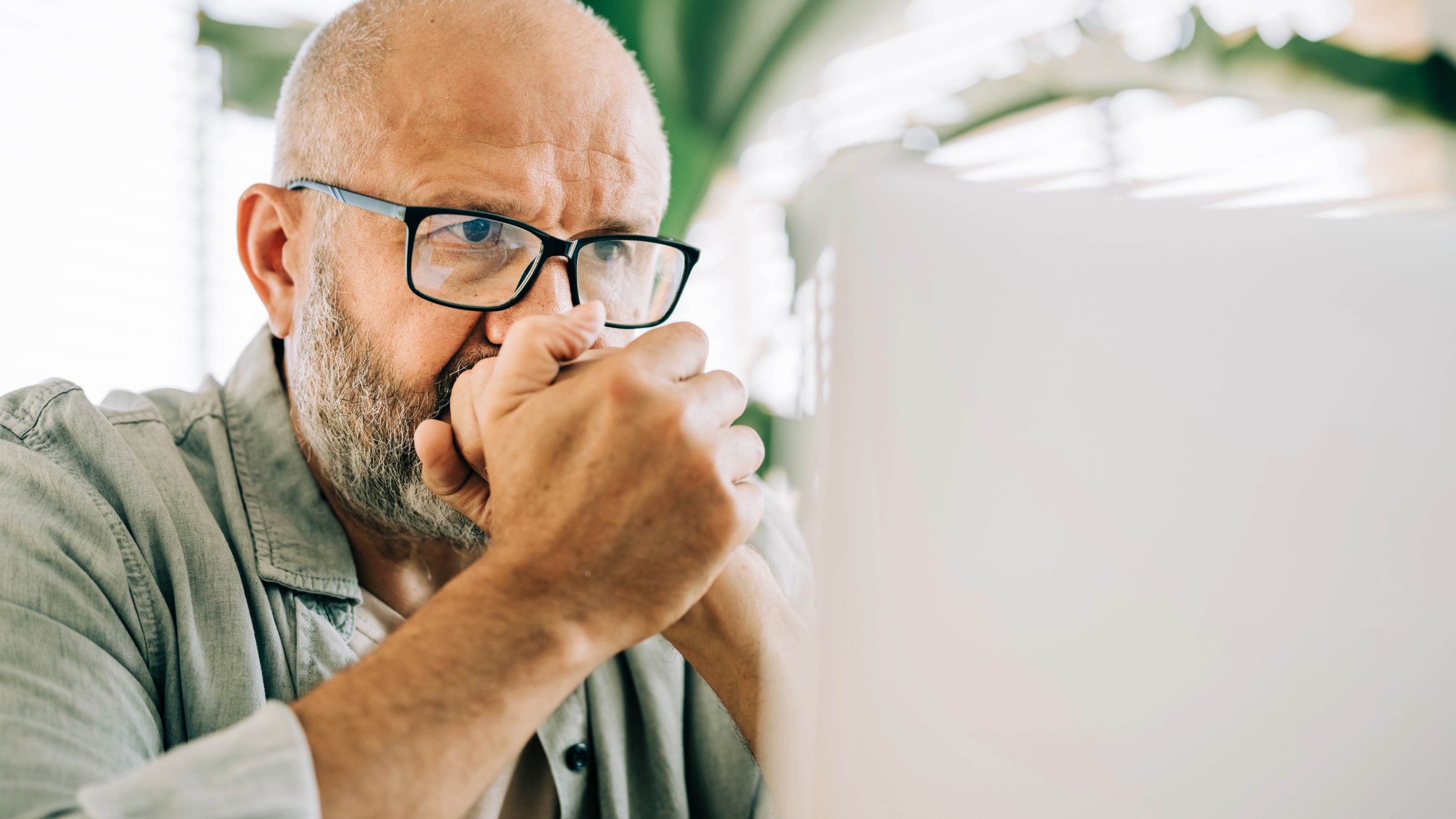 Close-up portrait of a worried middle-aged man looking at his laptop screen.
