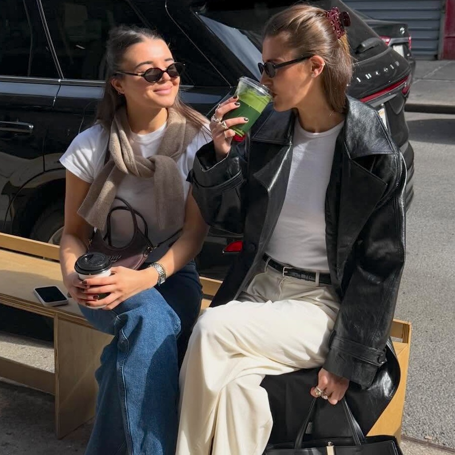 style influencer Coco Schiffer and her sister sit on a sidewalk bench in NYC wearing chic casual outfits for spring 2026 with white T-shirts