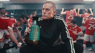 Channing Tatum holds a bottle of cold brew while crouched among a locker room of excited players in the Stōk Cold Brew 2025 Super Bowl Ad.