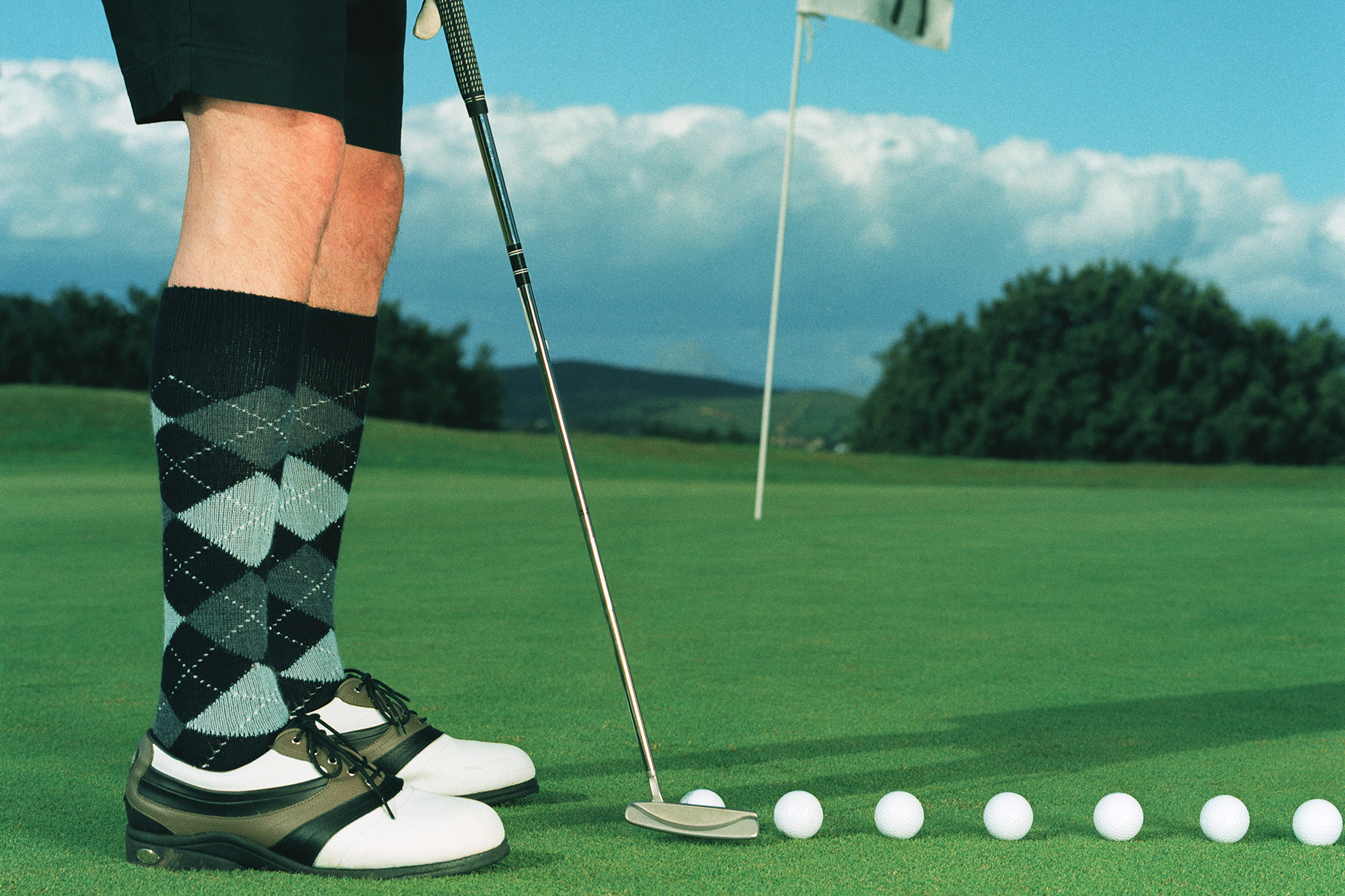 Golfer wearing long patterned golf socks with traditional golf shoes on the putting green