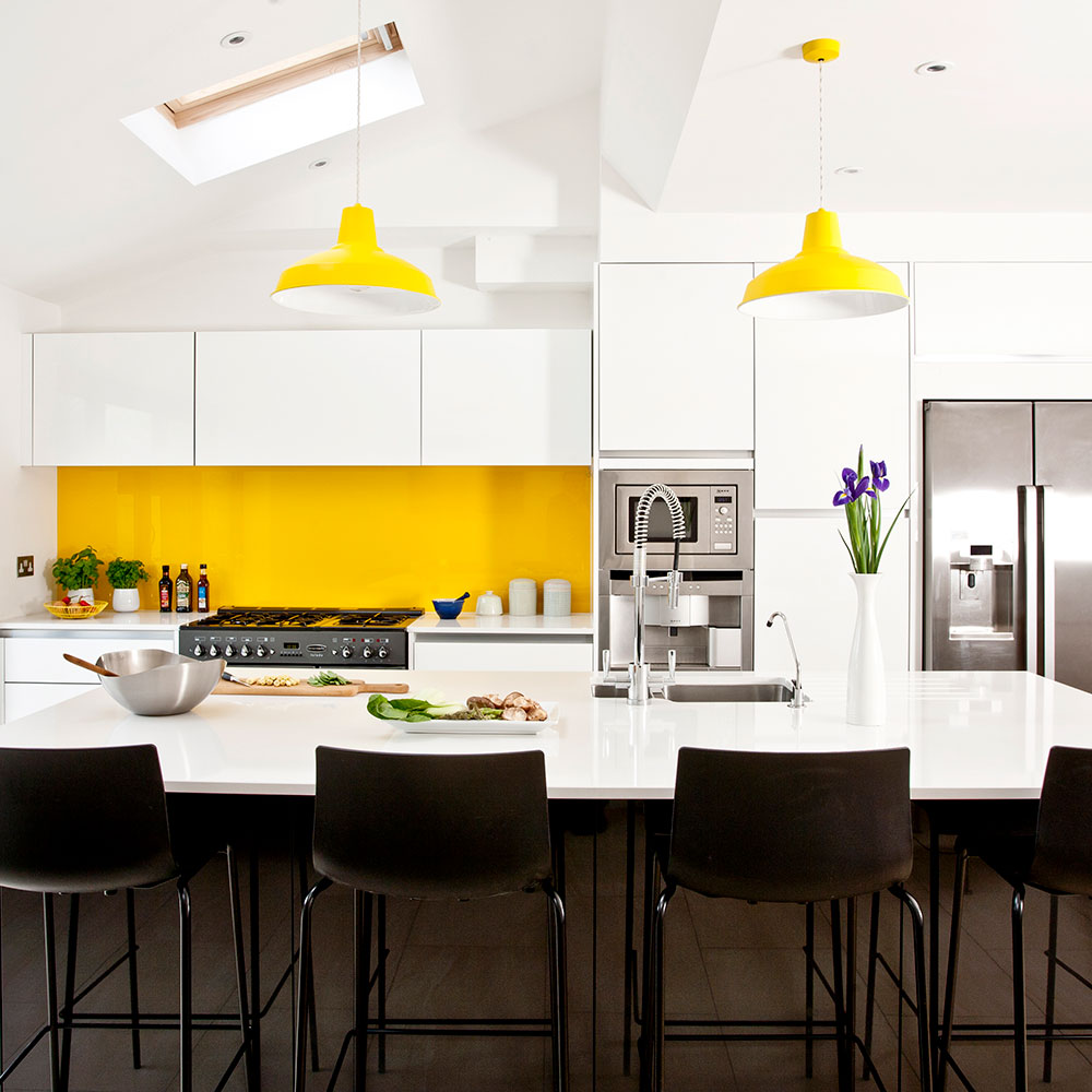White kitchen cabinets with a yellow splashback, yellow pendant lights and black bar stools