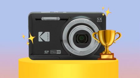 A Kodak Pixpro FZ55 compact camera with a zoom lens displayed on a pedestal, surrounded by stars and a trophy, set against a soft pastel background
