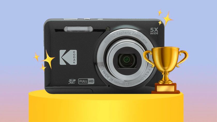 A Kodak Pixpro FZ55 compact camera with a zoom lens displayed on a pedestal, surrounded by stars and a trophy, set against a soft pastel background