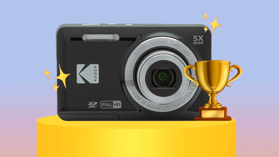 A Kodak Pixpro FZ55 compact camera with a zoom lens displayed on a pedestal, surrounded by stars and a trophy, set against a soft pastel background