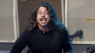 Dave Grohl performing onstage and playing guitar while sticking his tongue out. 