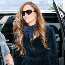 Jennifer Lopez steps out of a car wearing lace footless tights with a velvet tuxedo minidress and a Hermes bag.