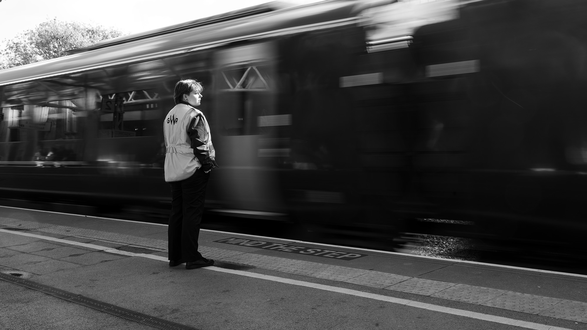 Black and white street photograph of train guard with train moving in background