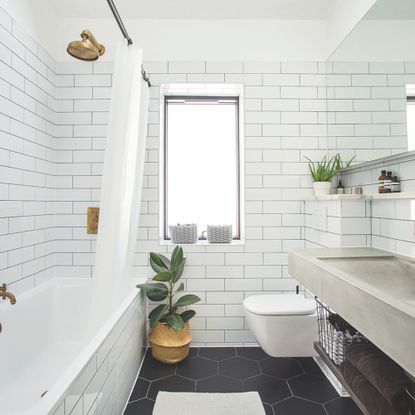 White tiled bathroom with black tiled floor, and brass taps and shower head in the bath