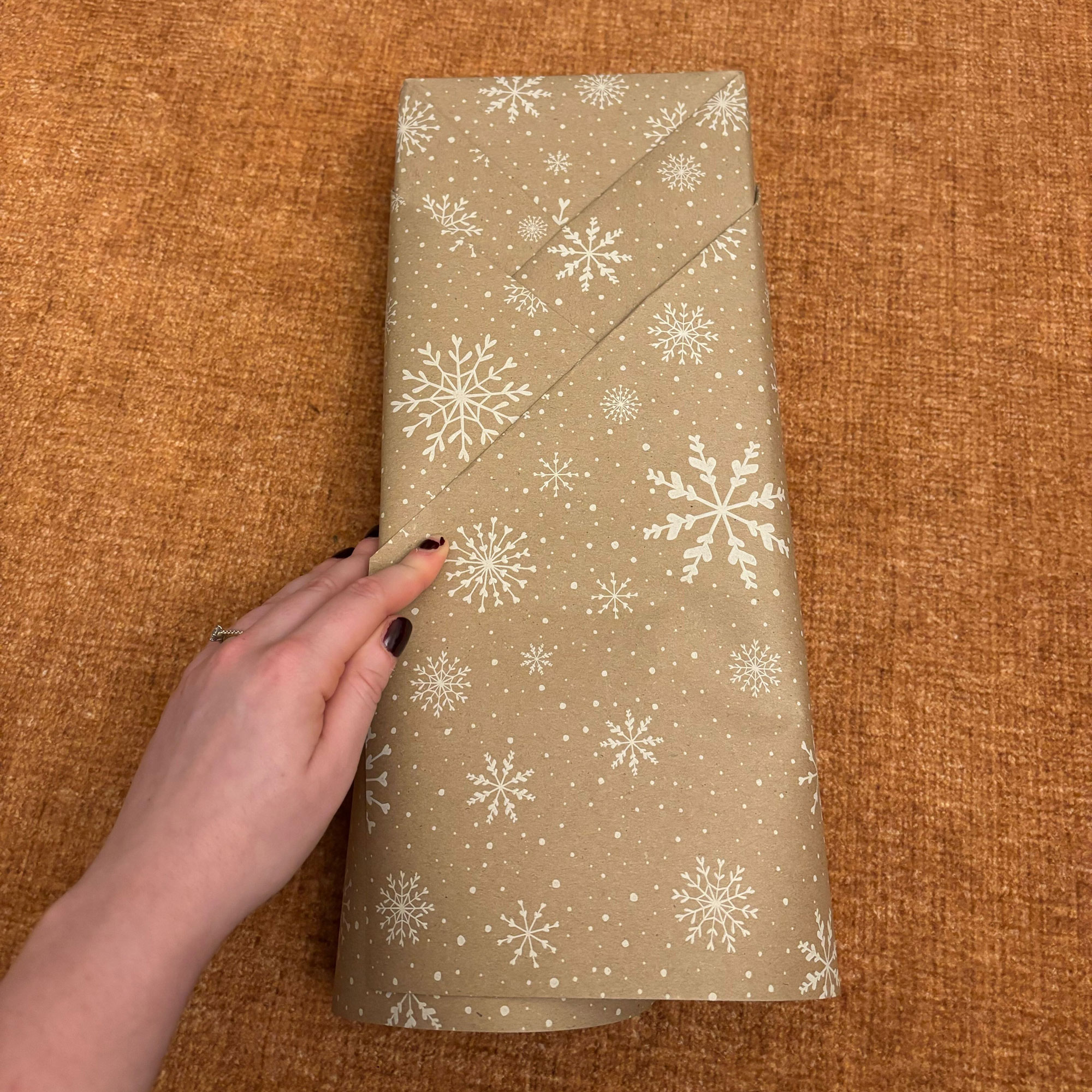 A rectangular box wrapped in brown paper with a white snowflake print on it