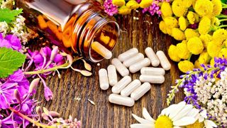 brown bottle of generic supplements spilled on table surrounded by flowers and herbs