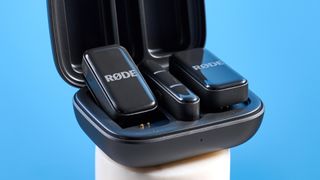 the rode wireless micro microphone with the black charging case and two black transmitter mics photographed against a blue background