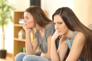 Two women sit on a couch, looking mad.