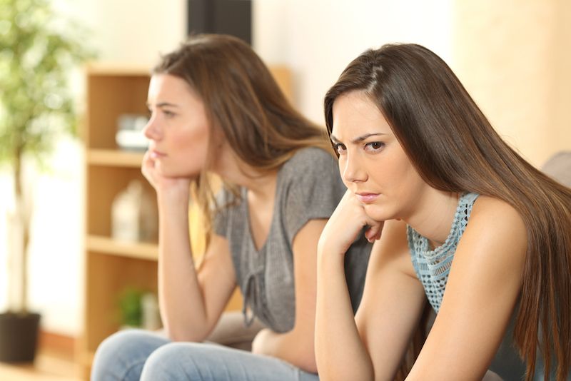 Two women sit on a couch, looking mad.