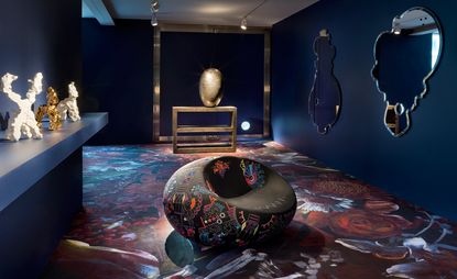 Dark flooring with mirrors on wall, abstract sculptures on side and round seat in middle
