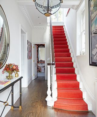 A hallway carpet idea with white walls and red carpet on the staircase