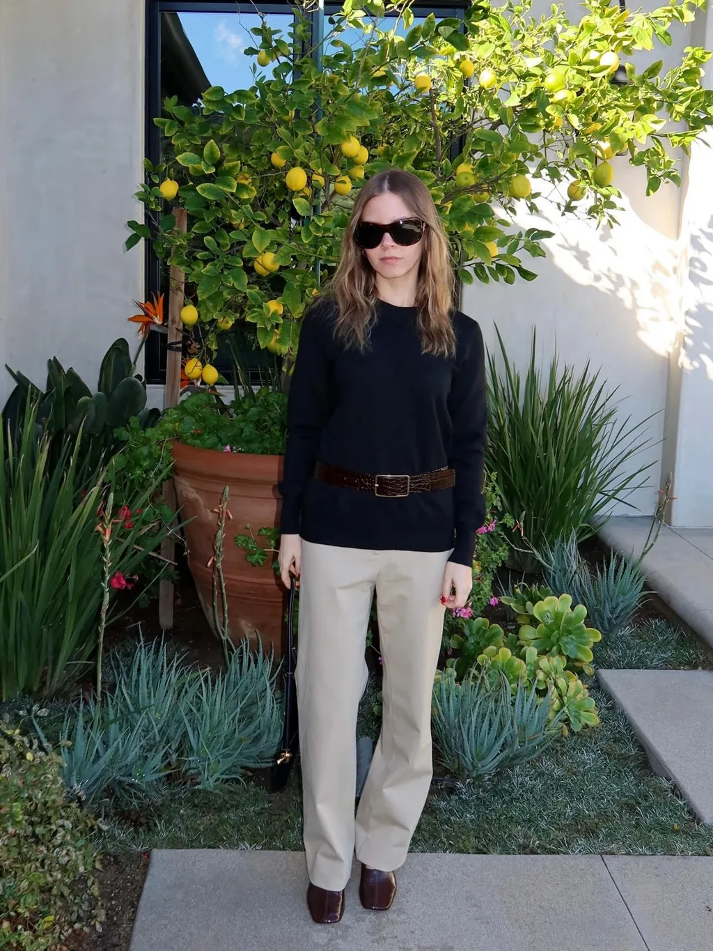 Nikki wears a black sweater with khaki pants, oversize sunglasses, and brown high-vamp pumps.