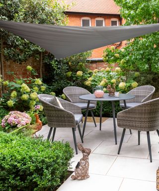 A gray garden table det with matching shade sale on a patio with hydrangea planting